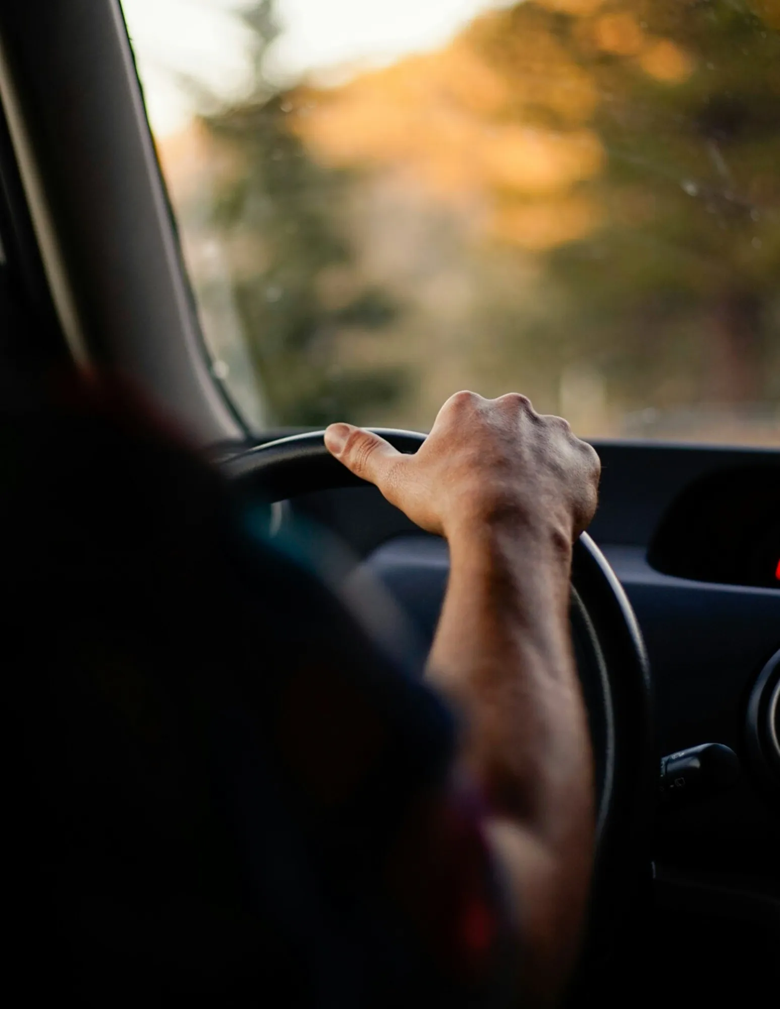 Una persona maneja un auto con la mano apoyada en el volante.